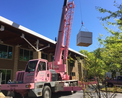 Pink crane lifting roofing materials to commercial site