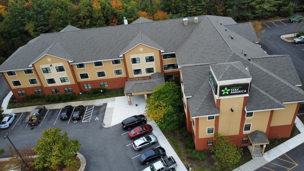 Aerial view of a completed commercial roofing project on a large hotel building surrounded by trees and parking lot