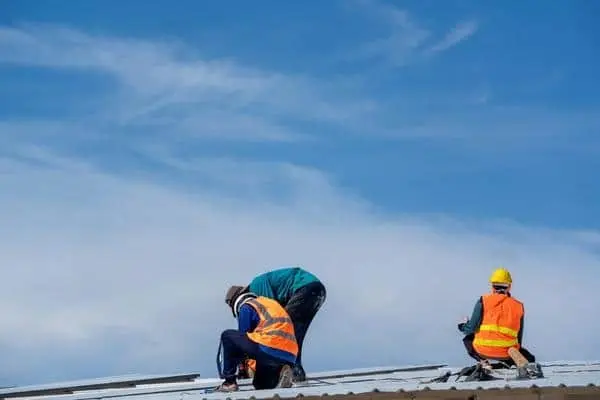 Two roofing contractors installing metal roofing panels on a commercial building under a clear sky in Atlanta